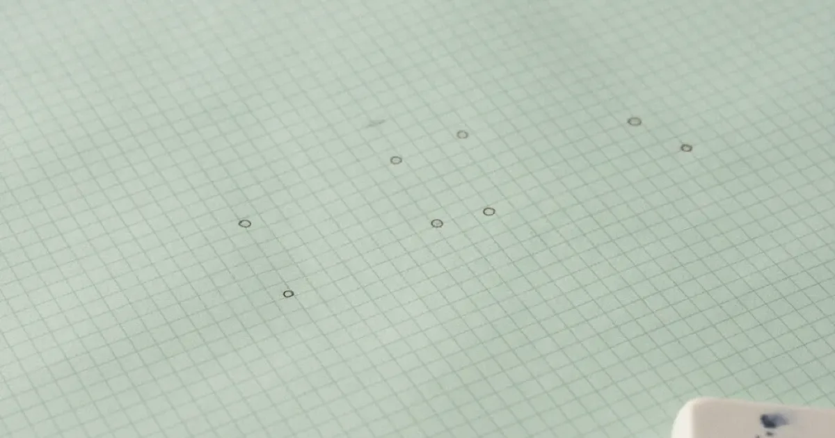 Papier millimétré vert pâle où des points ont été tracés au crayon, crayon taillé et gomme au bord